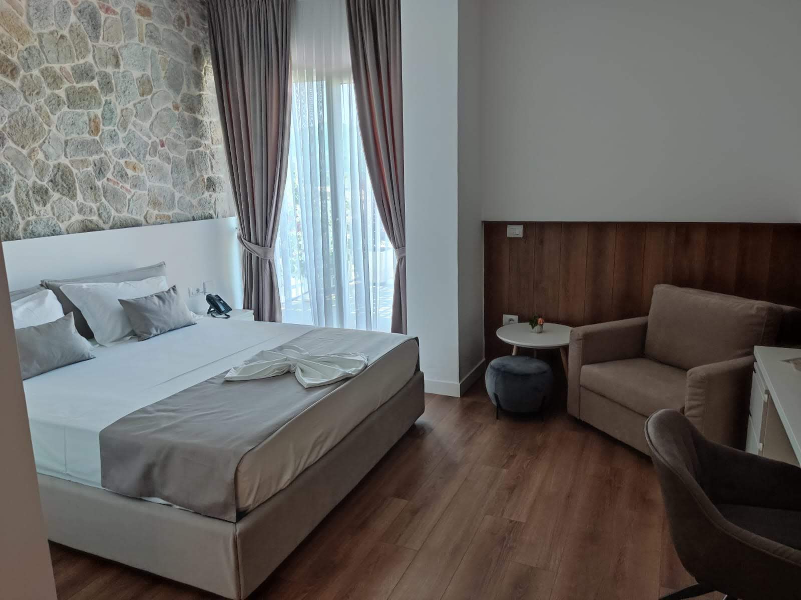 A room with a wooden floor, double bed and armchair